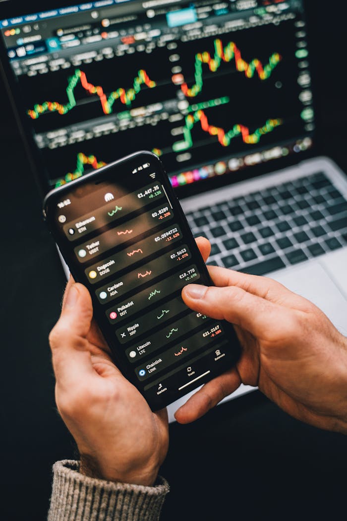 Home Hands holding smartphone with stock app, laptop displaying charts. Perfect for financial and technology themes.